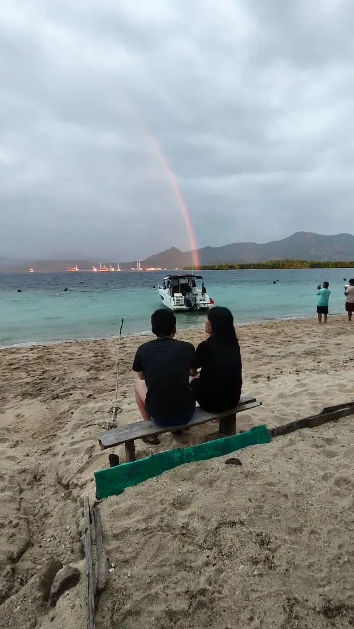 Couple watching a rainbow over the sea at sunset